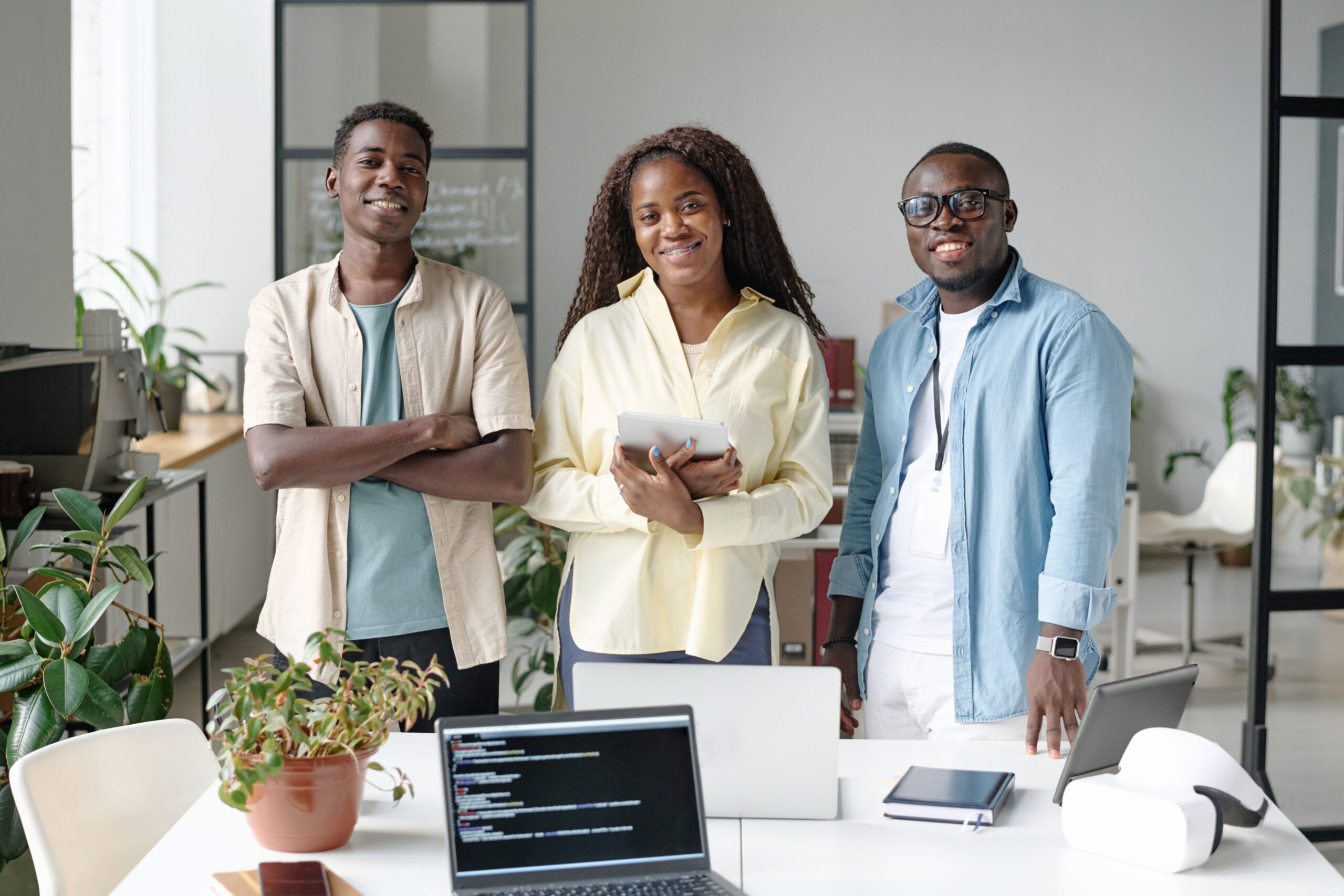 Portrait of African American young team of talented programmers standing next to work desk and smiling while looking at camera